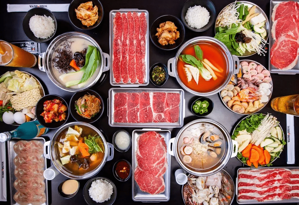 Six trays of meat and seafood with three trays of side dishes surrounding for pots of broth at Shabuya in Las Vegas