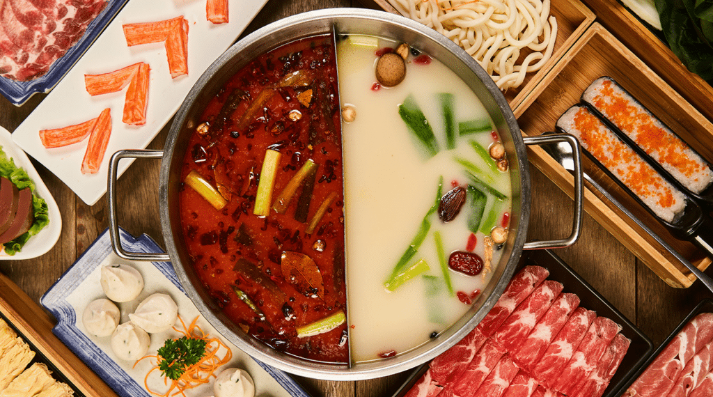 a pot with two different kinds of broth surrounded by side dishes and meat at Happy Lamb Hot Pot in Las Vegas